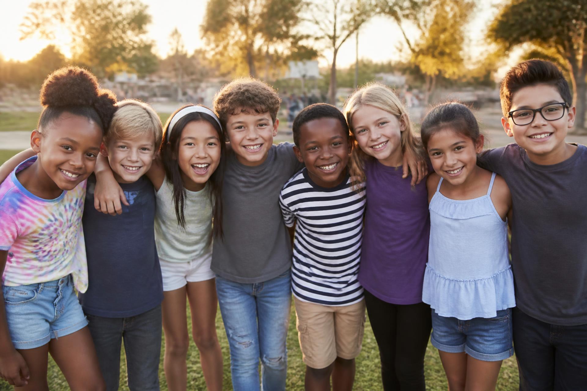 A group of smiling children of many races standing arm in arm together in a park